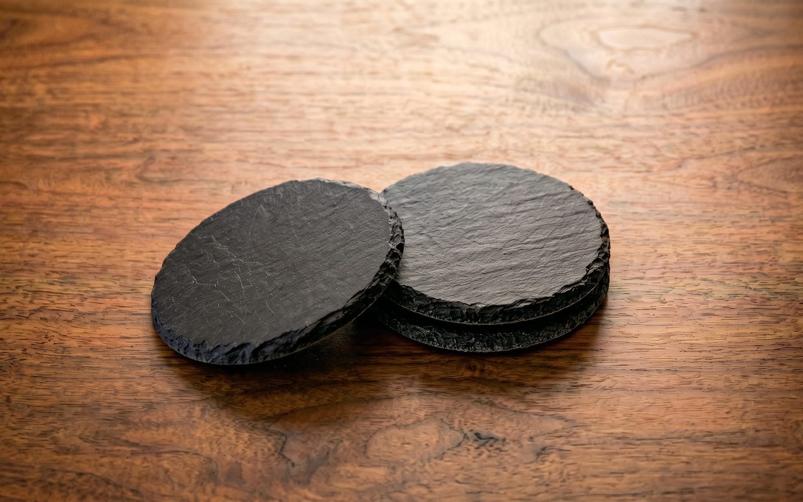 Stacked round slate coasters with chiselled edges on a walnut desk