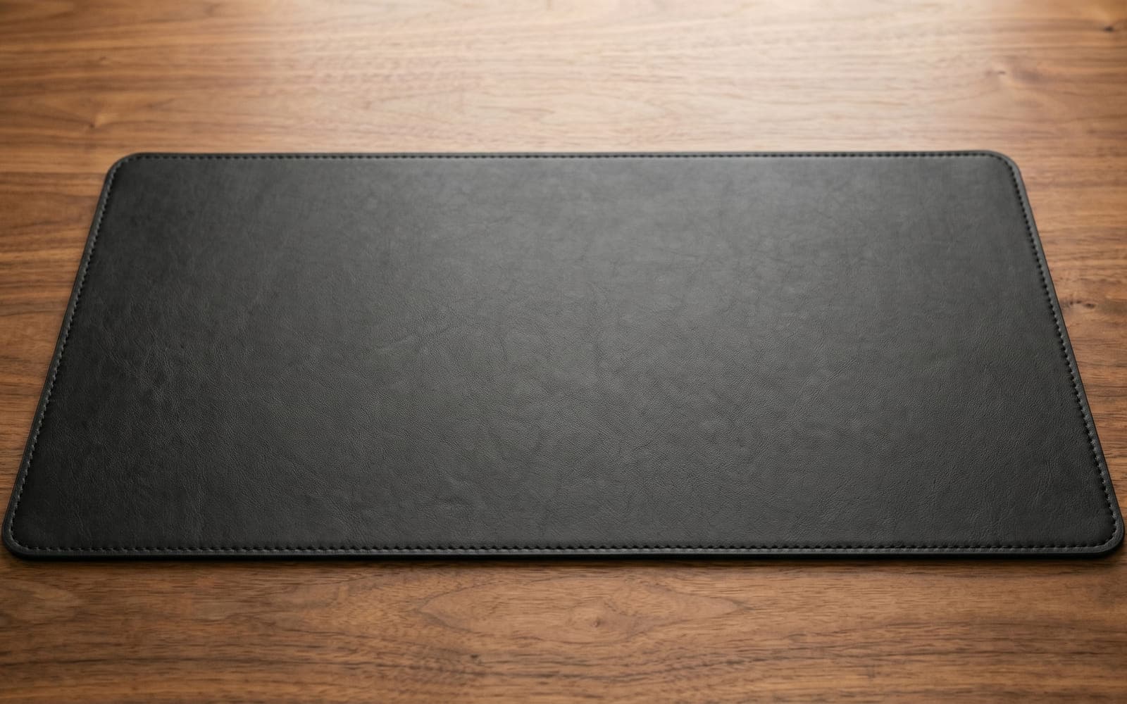 Black leather desk mat with stitched edges on a walnut desk