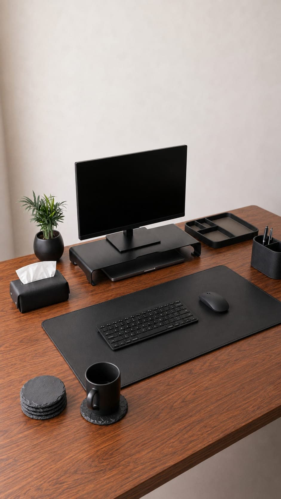 A walnut desk styled with a black leather mat, aluminium monitor riser, leather organizers, and slate coasters
