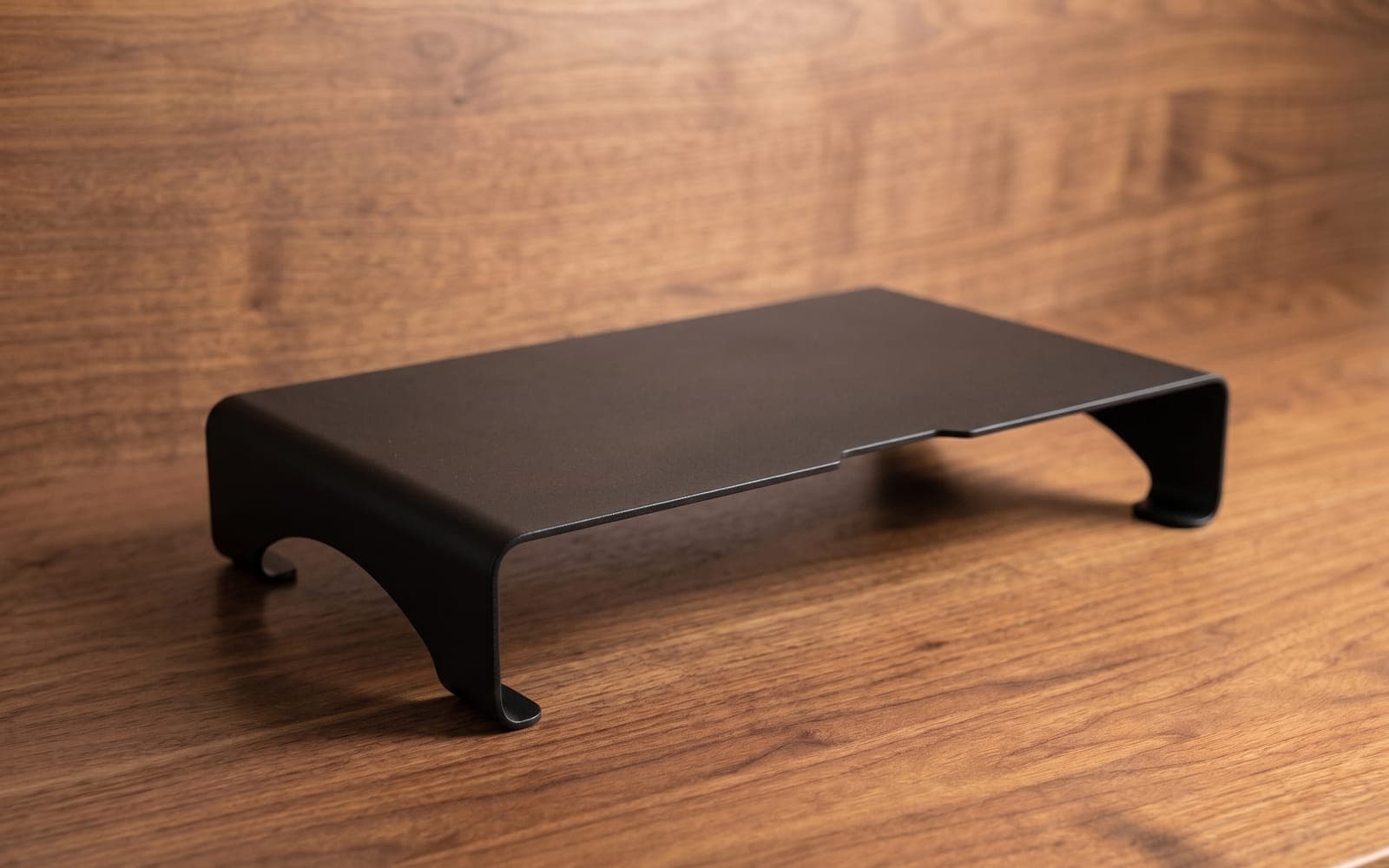 Black aluminium monitor riser on a walnut desk