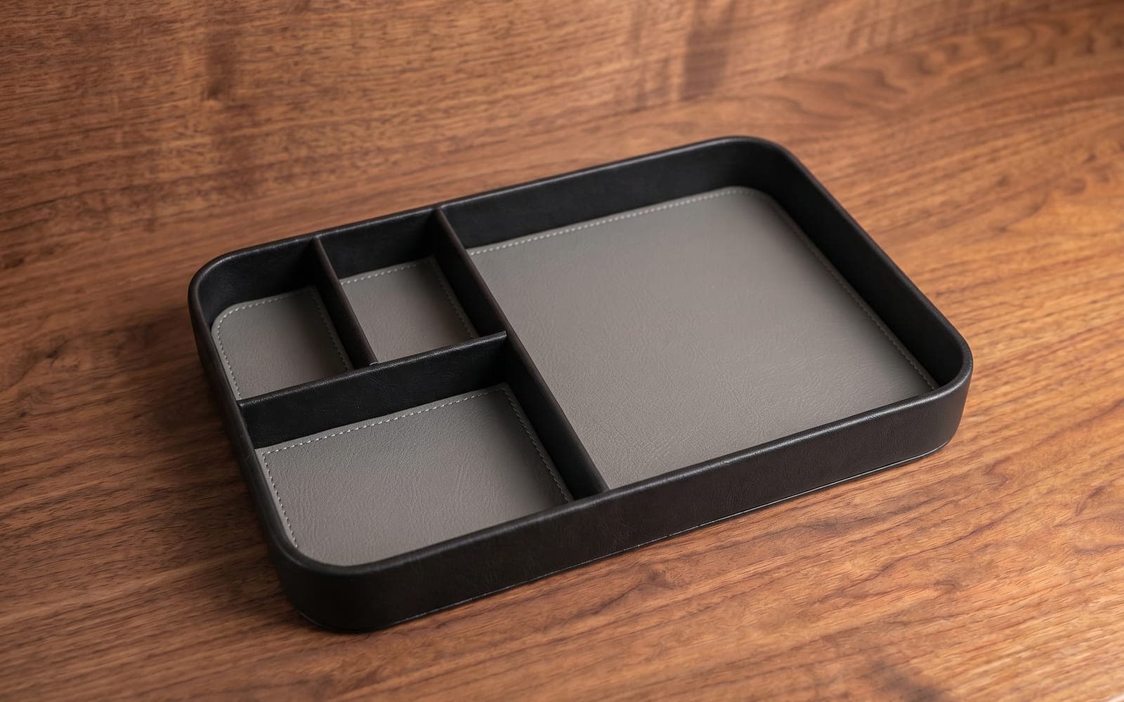 Black organizer tray with grey divided compartments on a walnut desk
