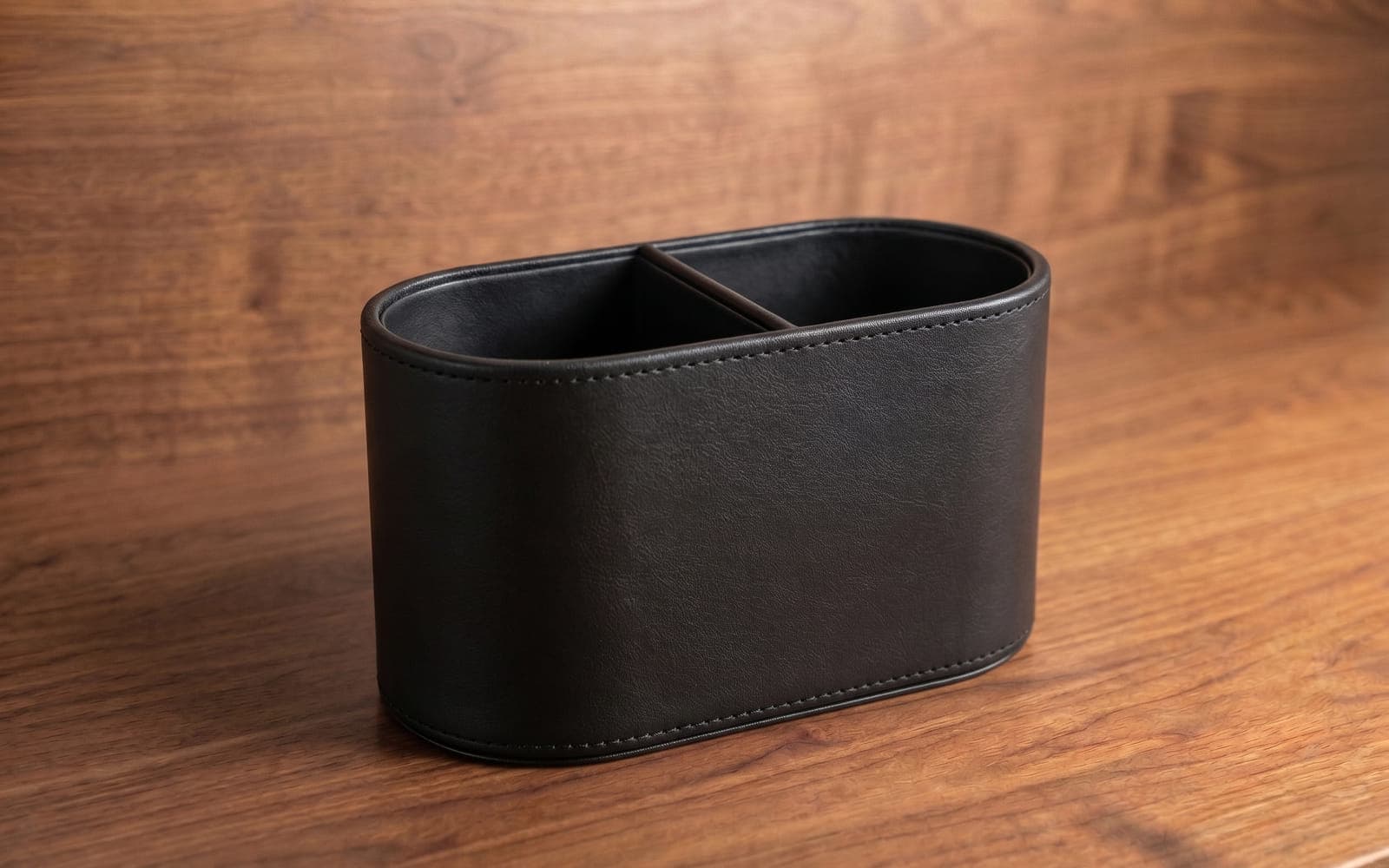 Black leather pen holder with two compartments on a walnut desk