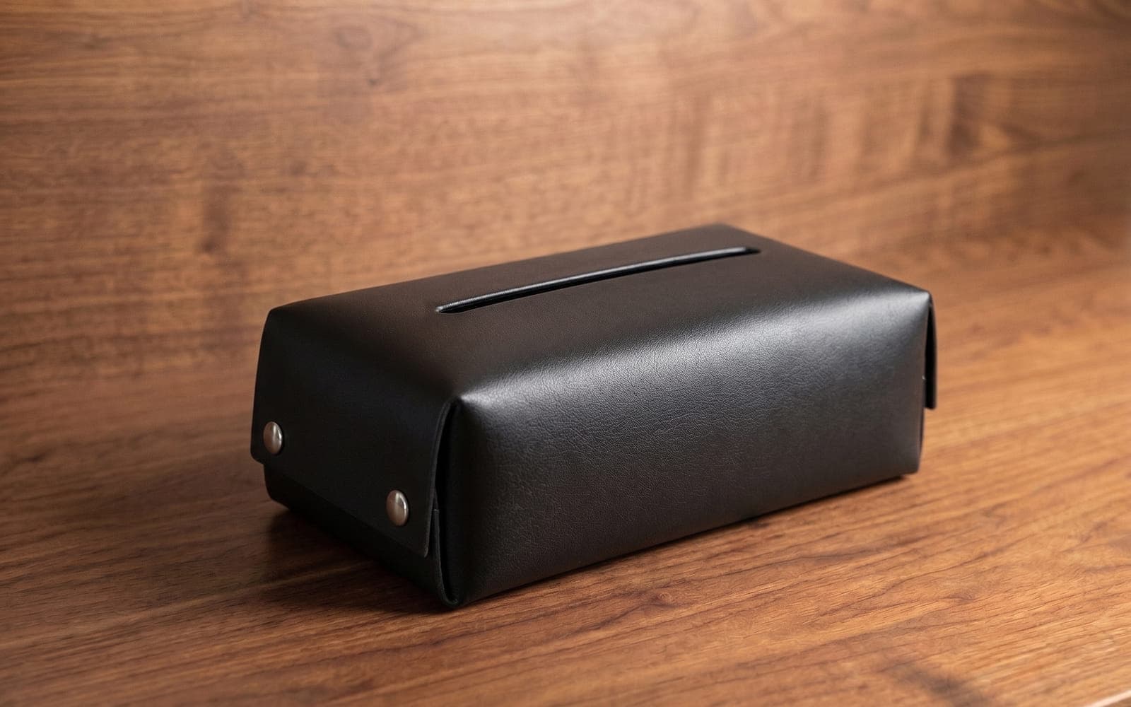 Black leather tissue box cover with metal studs on a walnut desk